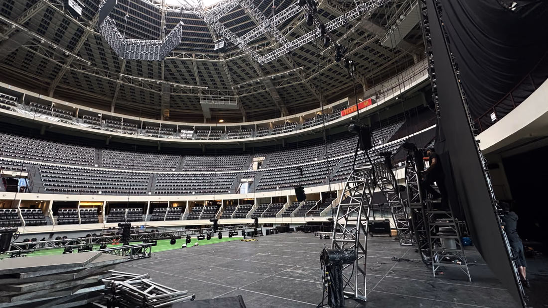 Arena vacía durante el montaje del escenario, con estructura de truss y equipo en el piso